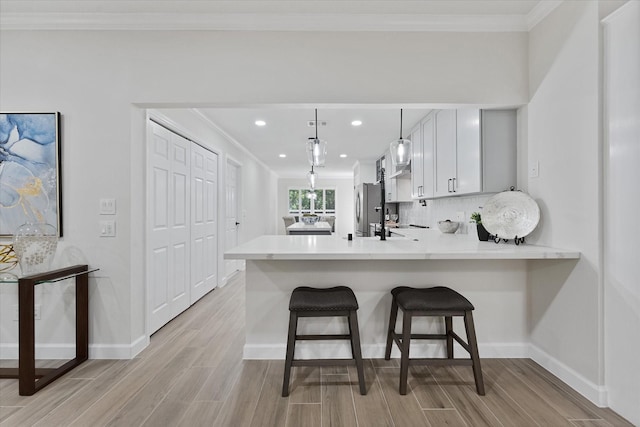 163 W Village Knoll Cir, The Woodlands, TX 77381 - kitchen with freestanding refrigerator, light wood-type flooring, a peninsula, light countertops, and ornamental molding