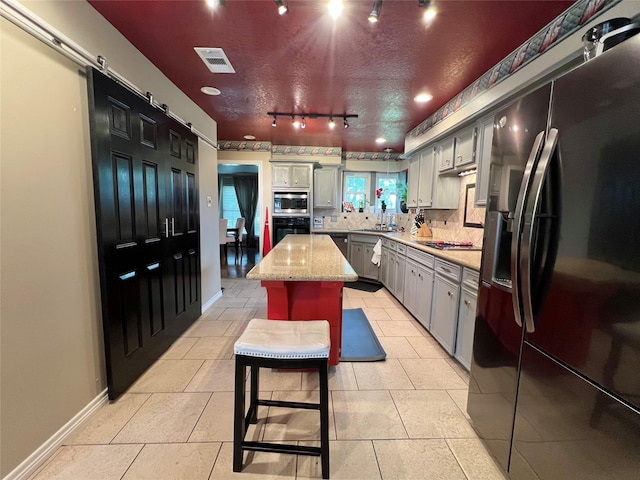 51 S Trillium Ct, Lake Jackson, TX 77566 - kitchen featuring black appliances, rail lighting, a barn door, decorative backsplash, and gray cabinets