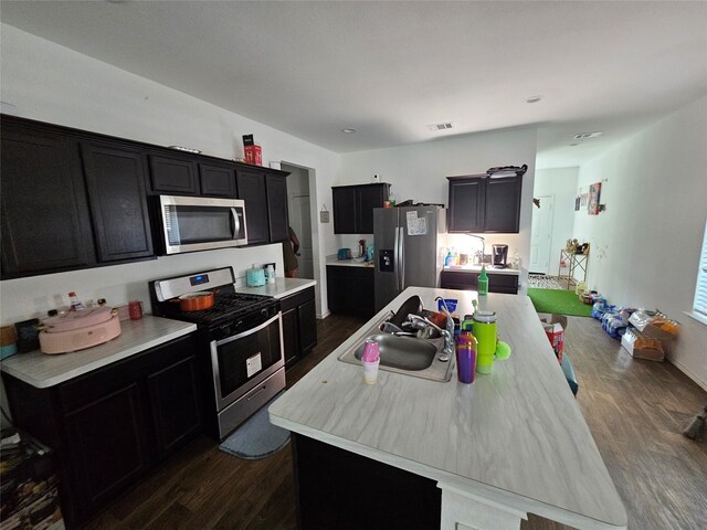 14902 Cypress Hollow Dr, Southeast Montgomery, TX 77357 - kitchen featuring appliances with stainless steel finishes, dark wood-style flooring, dark cabinetry, a kitchen island with sink, and light countertops