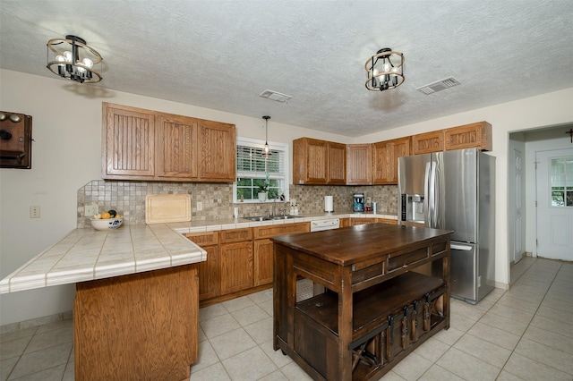 505 Sage Brush Dr, Somerville, TX 77879 - kitchen featuring stainless steel fridge with ice dispenser, a peninsula, backsplash, a chandelier, and tile countertops