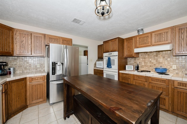 505 Sage Brush Dr, Somerville, TX 77879 - kitchen featuring white appliances, under cabinet range hood, light tile patterned floors, tasteful backsplash, and a textured ceiling