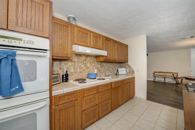 505 Sage Brush Dr, Somerville, TX 77879 - kitchen featuring under cabinet range hood, white appliances, decorative backsplash, a textured ceiling, and light tile patterned floors
