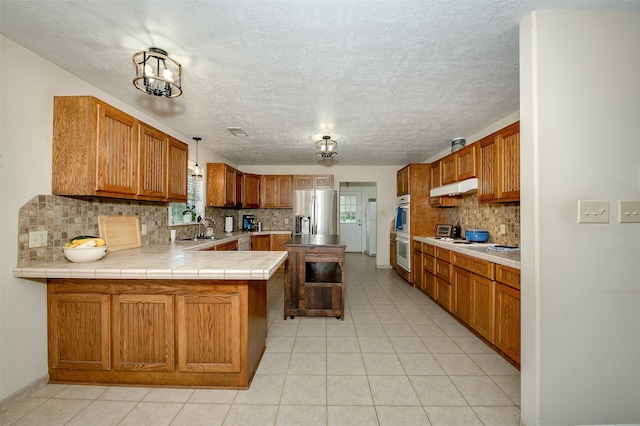 505 Sage Brush Dr, Somerville, TX 77879 - kitchen with white appliances, backsplash, a peninsula, under cabinet range hood, and light tile patterned floors