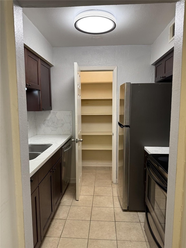 7555 Katy Fwy Unit 57, Houston, TX 77024 - kitchen featuring appliances with stainless steel finishes, dark brown cabinetry, light tile patterned flooring, a textured wall, and backsplash