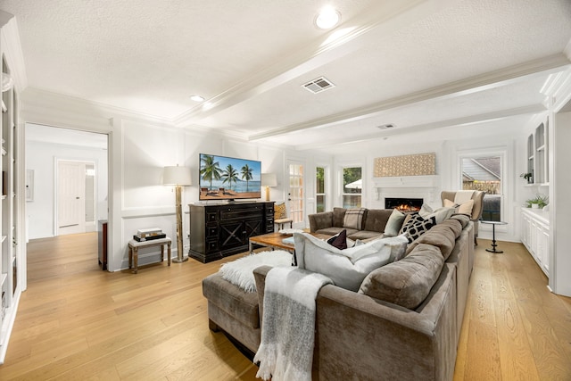 9727 Godstone Ln, Spring, TX 77379 - living area featuring light wood finished floors, beamed ceiling, a warm lit fireplace, crown molding, and a textured ceiling