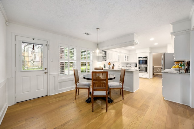 9727 Godstone Ln, Spring, TX 77379 - dining room featuring crown molding, a textured ceiling, light wood-style floors, a wainscoted wall, and a decorative wall
