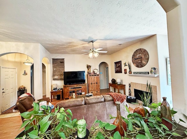 8010 N Tarrytown Crossing Dr, Conroe, TX 77304 - living room featuring arched walkways, a ceiling fan, a fireplace, a textured ceiling, and wood finished floors