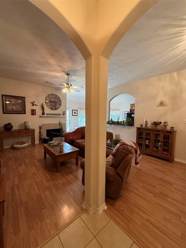 8010 N Tarrytown Crossing Dr, Conroe, TX 77304 - living room featuring ceiling fan, light wood-style flooring, a fireplace, a textured ceiling, and arched walkways