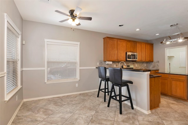 216 Willow Pointe Dr, League City, TX 77573 - kitchen with stainless steel microwave, tasteful backsplash, a ceiling fan, a peninsula, and brown cabinetry