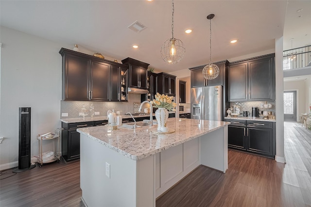 11527 Taagan Ln, Richmond, TX 77407 - kitchen with stainless steel fridge, dark wood-type flooring, a kitchen island with sink, decorative backsplash, and light stone countertops