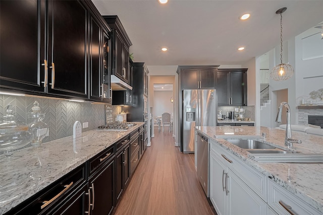 11527 Taagan Ln, Richmond, TX 77407 - kitchen featuring appliances with stainless steel finishes, light wood-type flooring, backsplash, light stone countertops, and dark cabinetry