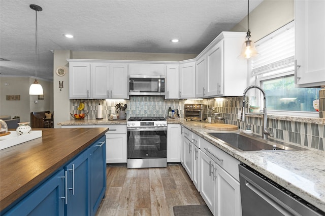 3926 Lavender St, Houston, TX 77026 - kitchen featuring stainless steel appliances, wooden counters, blue cabinets, white cabinetry, and a textured ceiling