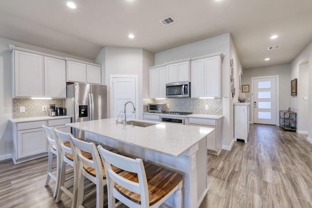 10026 Angelina Woods Ln, Conroe, TX 77384 - kitchen with appliances with stainless steel finishes, tasteful backsplash, a kitchen island with sink, light wood-style flooring, and a breakfast bar