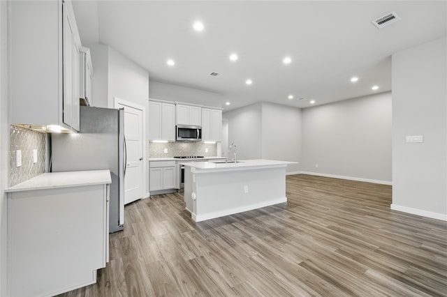 10026 Angelina Woods Ln, Conroe, TX 77384 - kitchen with appliances with stainless steel finishes, tasteful backsplash, light wood-style floors, a kitchen island with sink, and recessed lighting