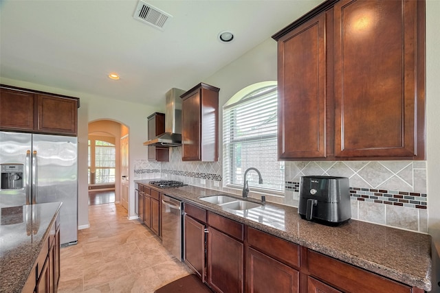 4311 Walden Terrace Ln, Humble, TX 77396 - kitchen featuring appliances with stainless steel finishes, arched walkways, wall chimney range hood, dark stone countertops, and backsplash