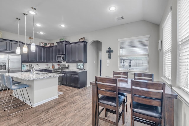 6423 Hunters Creek Ln, Baytown, TX 77521 - kitchen with appliances with stainless steel finishes, arched walkways, light stone countertops, light wood finished floors, and a center island with sink