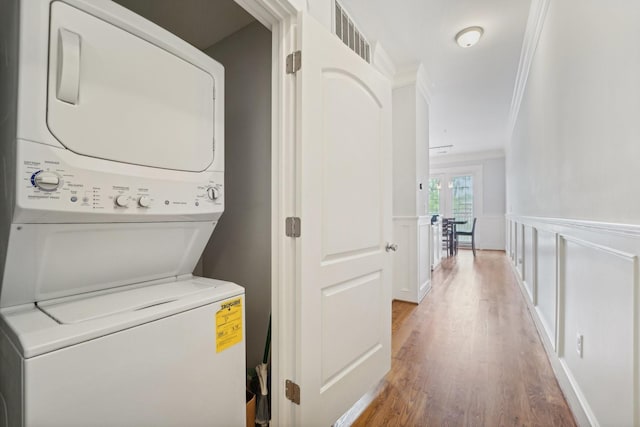 2802 Morrison St Unit 203, Houston, TX 77009 - laundry area featuring stacked washing machine and dryer, ornamental molding, light wood-style flooring, and wainscoting