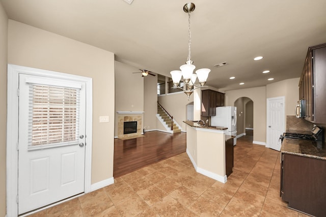 9119 Basin Ridge Ln, Richmond, TX 77407 - kitchen featuring arched walkways, white refrigerator with ice dispenser, dark brown cabinets, black gas range, and a tile fireplace