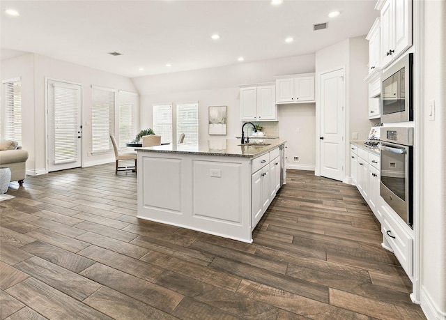 19002 Dublin Bay Blvd, Tomball, TX 77377 - kitchen featuring appliances with stainless steel finishes, white cabinetry, light stone countertops, a center island with sink, and dark wood-style flooring