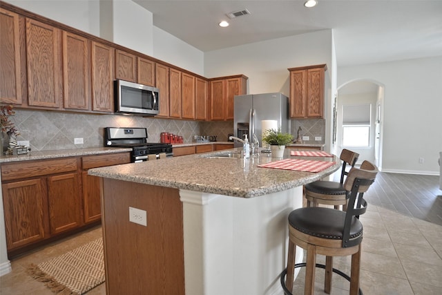 12421 Berberry Dr, Texas City, TX 77568 - kitchen featuring appliances with stainless steel finishes, arched walkways, a breakfast bar, brown cabinets, and backsplash