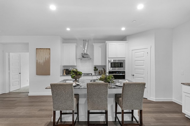 3913 Silver Fls, League City, TX 77573 - kitchen featuring stainless steel appliances, wall chimney exhaust hood, a breakfast bar, white cabinetry, and recessed lighting