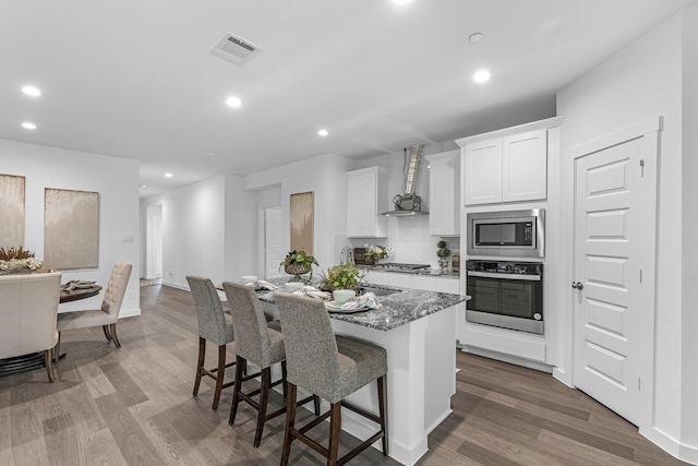 3913 Silver Fls, League City, TX 77573 - kitchen with stainless steel appliances, wall chimney exhaust hood, an island with sink, dark wood-style flooring, and a breakfast bar area