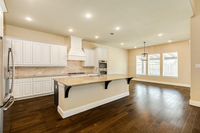10306 Terra St, Iowa Colony, TX 77583 - kitchen with custom range hood, stainless steel appliances, backsplash, light stone counters, and white cabinetry
