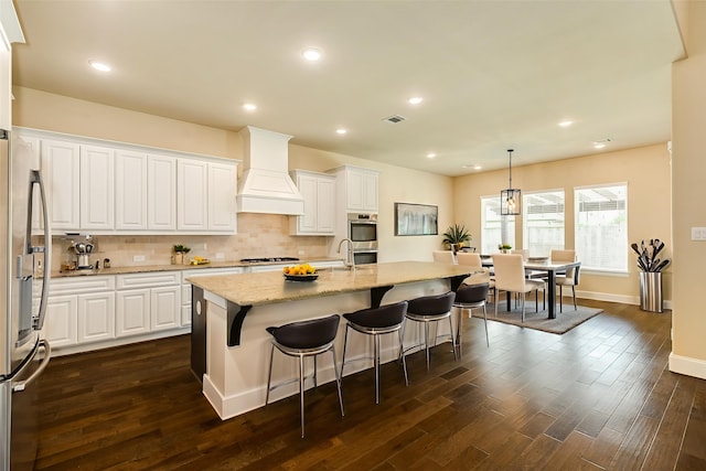 10306 Terra St, Iowa Colony, TX 77583 - kitchen with premium range hood, stainless steel appliances, dark wood finished floors, white cabinets, and decorative backsplash