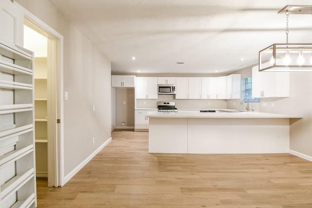 7602 12th Fairway Ln, Humble, TX 77346 - kitchen featuring appliances with stainless steel finishes, white cabinetry, light countertops, light wood-style flooring, and a peninsula
