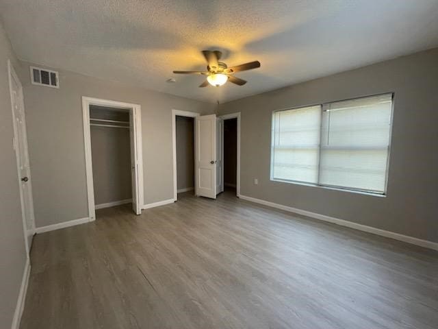 1114 E Pecan St, Angleton, TX 77515 - unfurnished bedroom with multiple closets, wood finished floors, a ceiling fan, and a textured ceiling