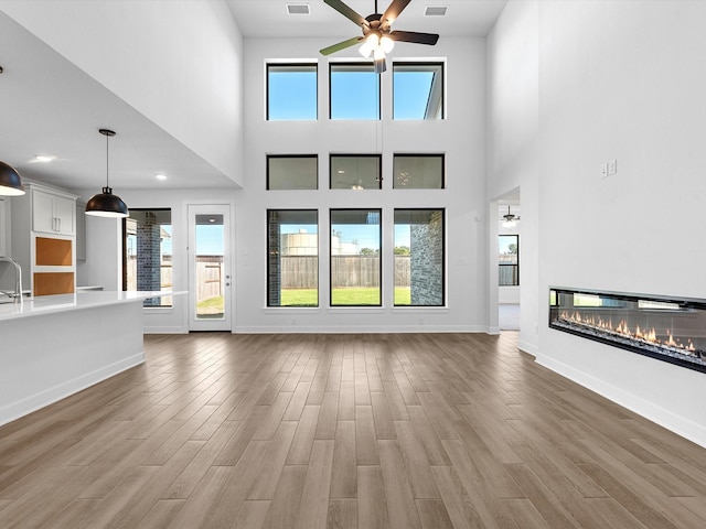 10806 Capella Creek Way, Richmond, TX 77406 - unfurnished living room featuring ceiling fan, light wood-style floors, a glass covered fireplace, plenty of natural light, and a towering ceiling