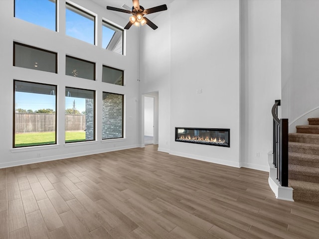 10806 Capella Creek Way, Richmond, TX 77406 - unfurnished living room with stairs, wood finished floors, a towering ceiling, a ceiling fan, and a glass covered fireplace