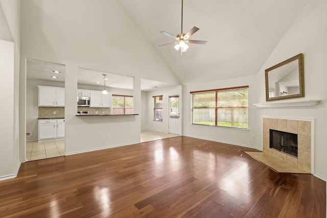 16210 Bloom Meadow Trl, Cypress, TX 77433 - unfurnished living room featuring a ceiling fan, light wood-style flooring, a tiled fireplace, and high vaulted ceiling