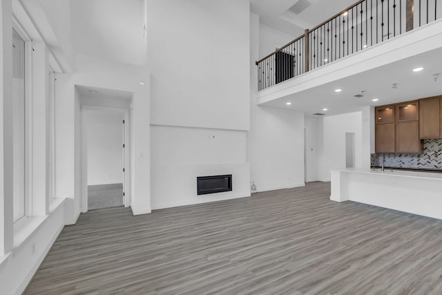 15643 Thirsty Horse Trl, Cypress, TX 77433 - unfurnished living room featuring a towering ceiling, light wood finished floors, a glass covered fireplace, and recessed lighting