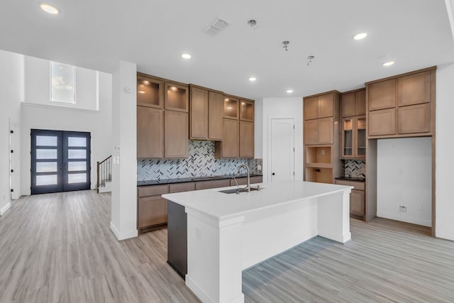 15643 Thirsty Horse Trl, Cypress, TX 77433 - kitchen with brown cabinetry, a center island with sink, french doors, light wood-style floors, and tasteful backsplash