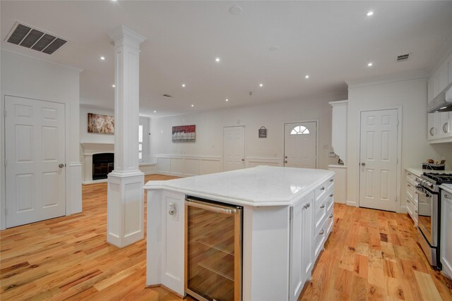 4400 Edith St, Bellaire, TX 77401 - kitchen featuring wine cooler, stainless steel range with gas cooktop, ornate columns, white cabinets, and a kitchen island
