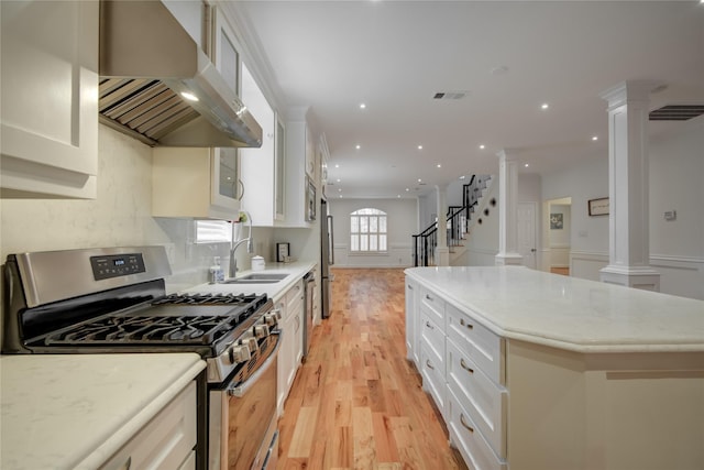 4400 Edith St, Bellaire, TX 77401 - kitchen featuring stainless steel appliances, range hood, ornate columns, light wood-style floors, and open floor plan