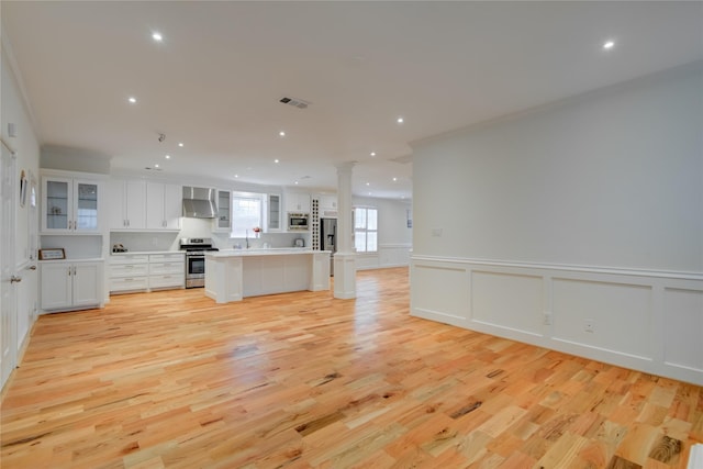 4400 Edith St, Bellaire, TX 77401 - kitchen with wall chimney range hood, stainless steel appliances, open floor plan, decorative columns, and light wood-style floors