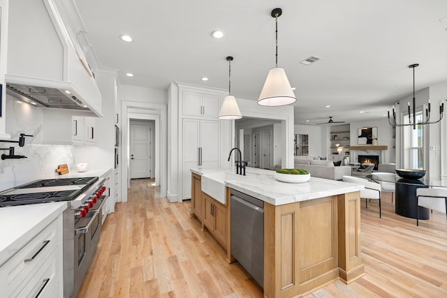 4902 Oak Forest Dr, Houston, TX 77018 - kitchen with appliances with stainless steel finishes, light wood-style floors, recessed lighting, a kitchen island with sink, and a warm lit fireplace
