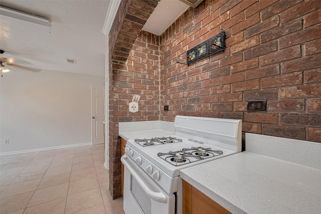21319 Park Mill Dr, Katy, TX 77450 - kitchen featuring white gas range oven, brick wall, light countertops, ceiling fan, and light tile patterned floors