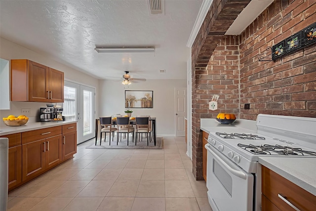 21319 Park Mill Dr, Katy, TX 77450 - kitchen with white gas stove, brown cabinets, ceiling fan, brick wall, and light countertops