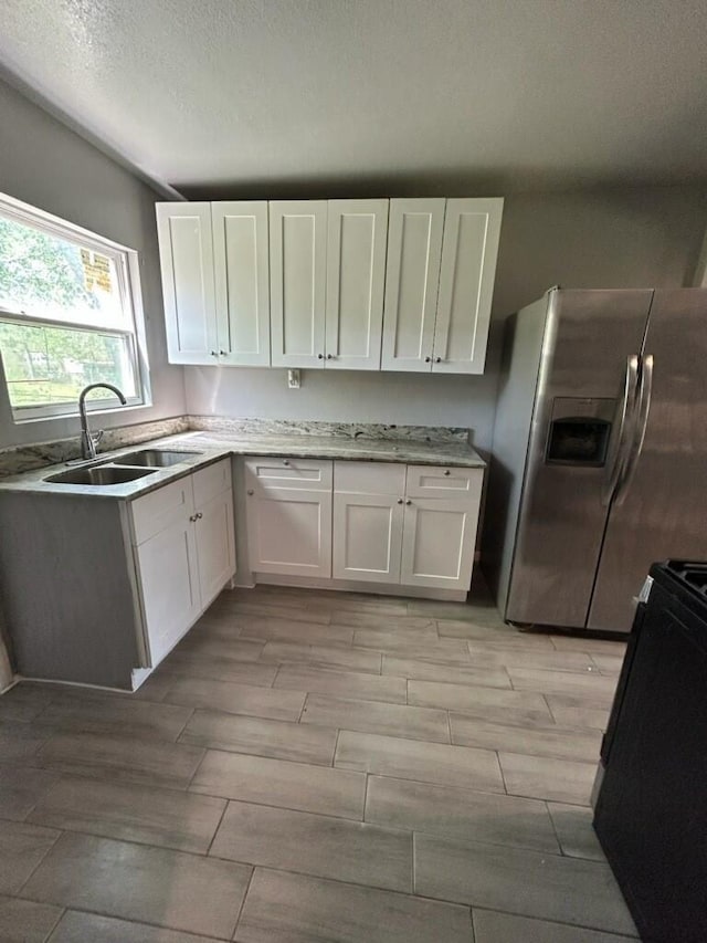 1108 Niagara St, Houston, TX 77051 - kitchen featuring stainless steel fridge, black range oven, white cabinetry, wood finish floors, and a textured ceiling
