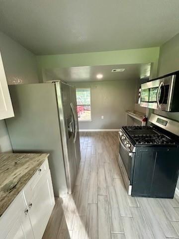 1108 Niagara St, Houston, TX 77051 - kitchen featuring stainless steel appliances, wood tiled floors, white cabinets, and light stone countertops
