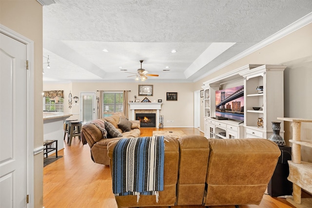 24418 Okehampton Dr, Tomball, TX 77375 - living area featuring light wood-style floors, ceiling fan, a raised ceiling, a textured ceiling, and a warm lit fireplace