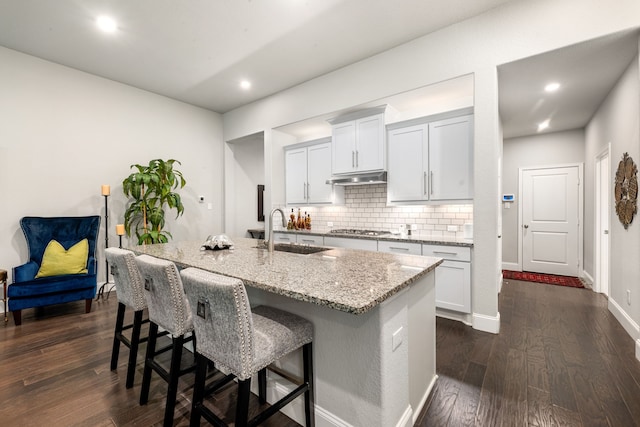27688 Vivace Dr, Spring, TX 77386 - kitchen with stainless steel gas cooktop, backsplash, a breakfast bar area, light stone countertops, and dark wood finished floors
