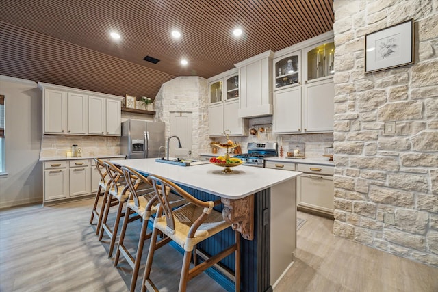 7203 Mayapple Grove Ln, Katy, TX 77493 - kitchen featuring appliances with stainless steel finishes, light countertops, a center island with sink, a kitchen bar, and light wood-style floors