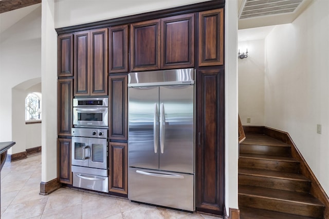 19216 Fm 442nd Rd, Needville, TX 77461 - kitchen featuring stainless steel appliances, a warming drawer, arched walkways, light tile patterned floors, and dark brown cabinetry