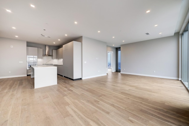 1711 Allen Pkwy Unit 2203, Houston, TX 77019 - kitchen featuring wall chimney range hood, modern cabinets, light wood finished floors, a center island with sink, and light countertops