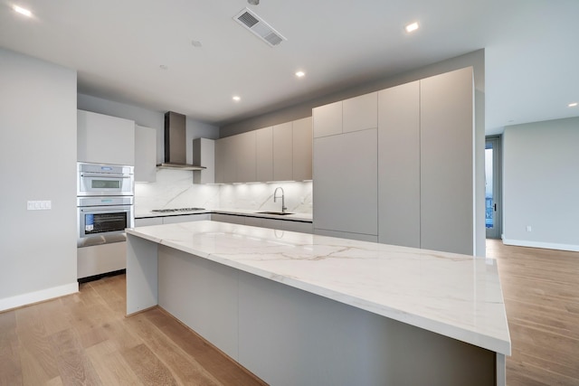 1711 Allen Pkwy Unit 2203, Houston, TX 77019 - kitchen with wall chimney range hood, stovetop, light wood finished floors, light stone countertops, and recessed lighting