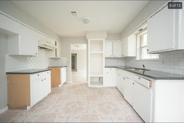 12911 Slater Ln, Houston, TX 77039 - kitchen with backsplash, under cabinet range hood, dark countertops, light tile patterned floors, and white cabinets